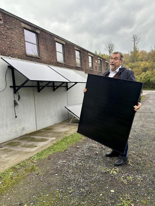 Journaliste de la RTBF tenant un panneau solaire 200 Wc devant les locaux de Wattuneed, avec en arrière-plan un système plug and play