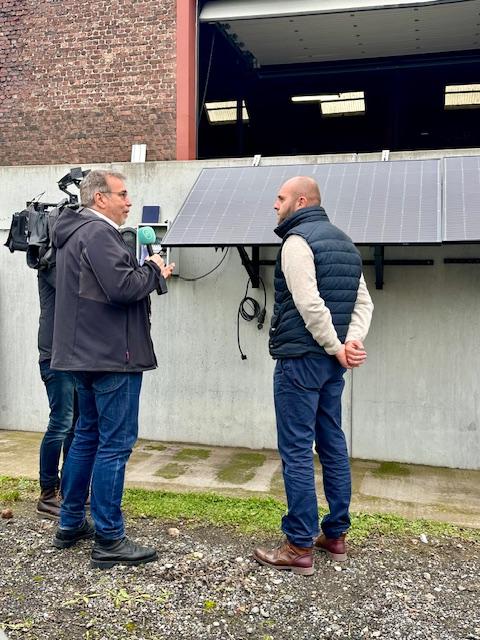 Julien Mawet avec un cameraman et un journaliste de la RTBF, à l'extérieur devant les locaux de Wattuneed, avec des panneaux solaires plug and play en arrière-plan
