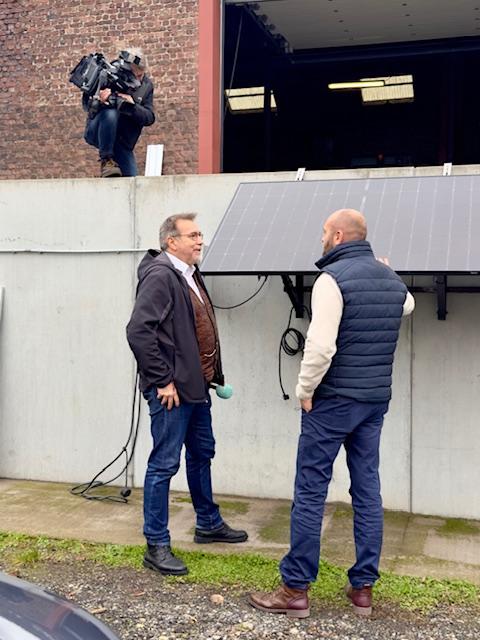 Julien Mawet avec un cameraman et un journaliste de la RTBF, à l'extérieur devant les locaux de Wattuneed, avec des panneaux solaires plug and play en arrière-plan