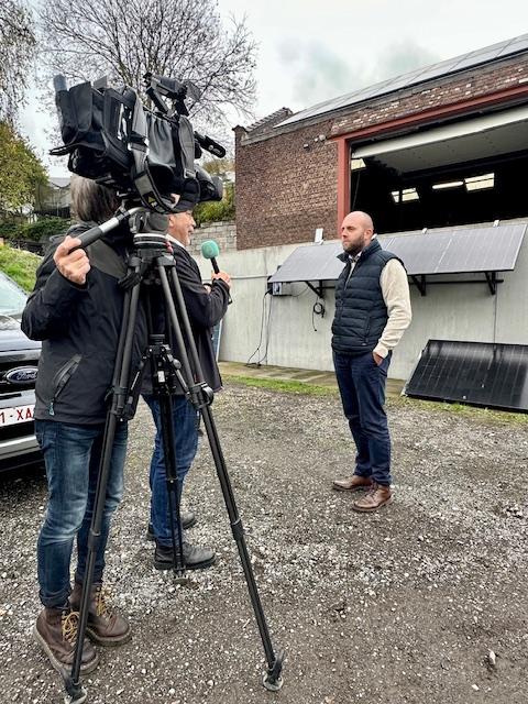 Julien Mawet avec un cameraman et un journaliste de la RTBF, à l'extérieur devant les locaux de Wattuneed, avec des panneaux solaires plug and play en arrière-plan