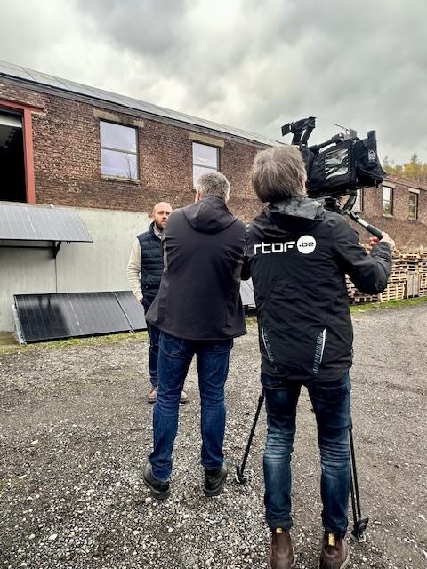 Julien Mawet avec un cameraman et un journaliste de la RTBF, à l'extérieur devant les locaux de Wattuneed, avec des panneaux solaires plug and play en arrière-plan