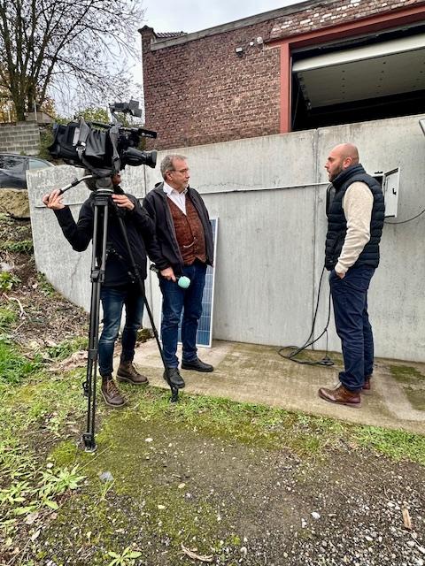 Julien Mawet avec un cameraman et un journaliste de la RTBF, à l'extérieur devant les locaux de Wattuneed, avec des panneaux solaires plug and play en arrière-plan